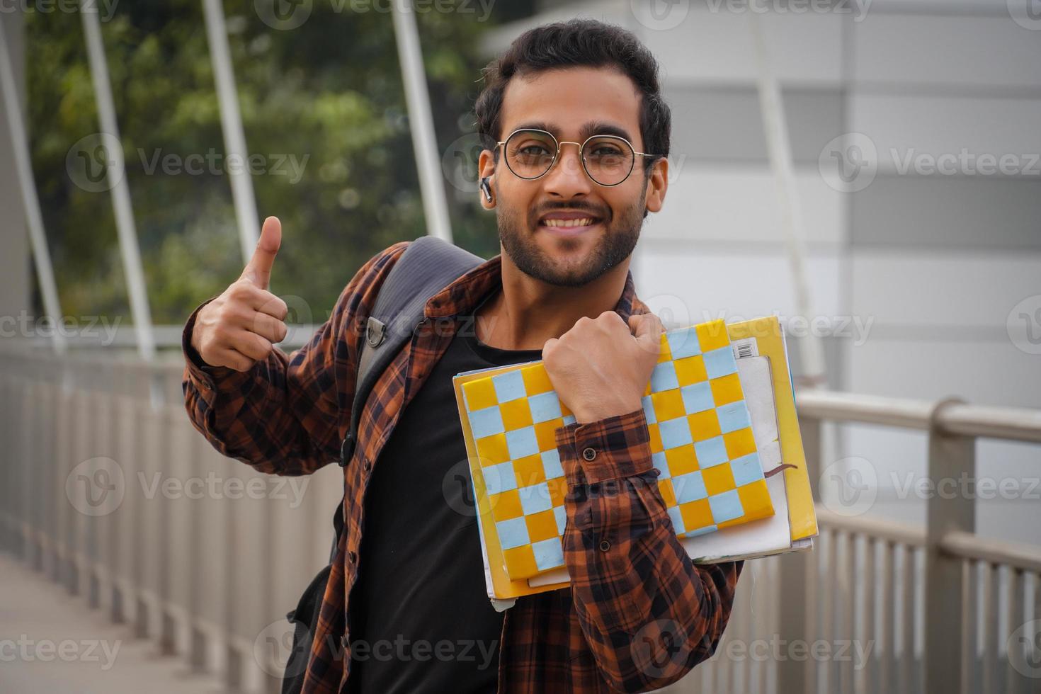 étudiant donnant les pouces vers le haut ayant un sac de sable de livre et près de l'image du campus universitaire photo