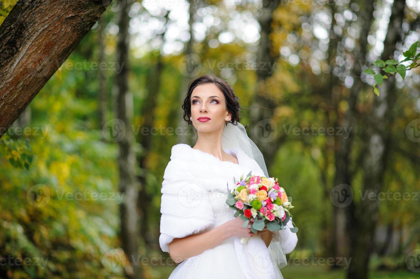 portrait d'une mariée solitaire sur fond de parc d'automne. la jeune fille s'est réfugiée sous un voile avec lequel le vent se développe. photo