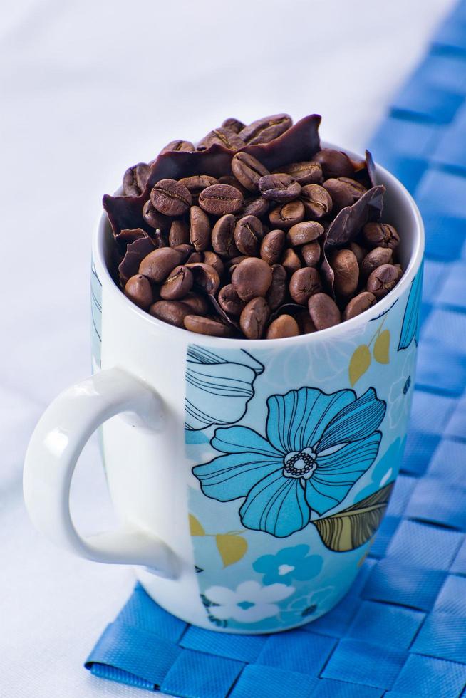 tasse blanche avec des grains de café et des morceaux de chocolat noir sur une nappe blanche photo