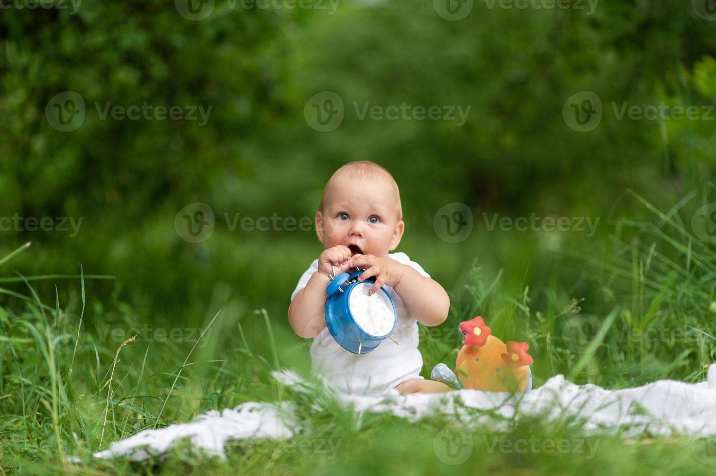 portrait d'un petit garçon mignon dans un parc sur la nature. tourné entouré de verdure. le garçon est joué par une horloge antique. photo