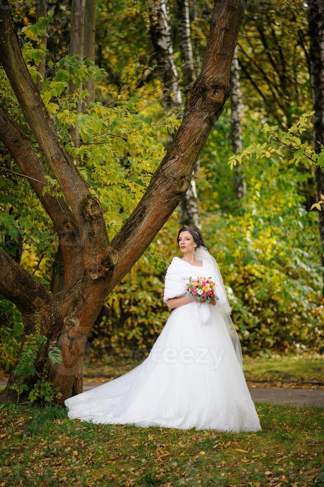 portrait d'une mariée solitaire sur fond de parc d'automne. la jeune fille s'est réfugiée sous un voile avec lequel le vent se développe. photo