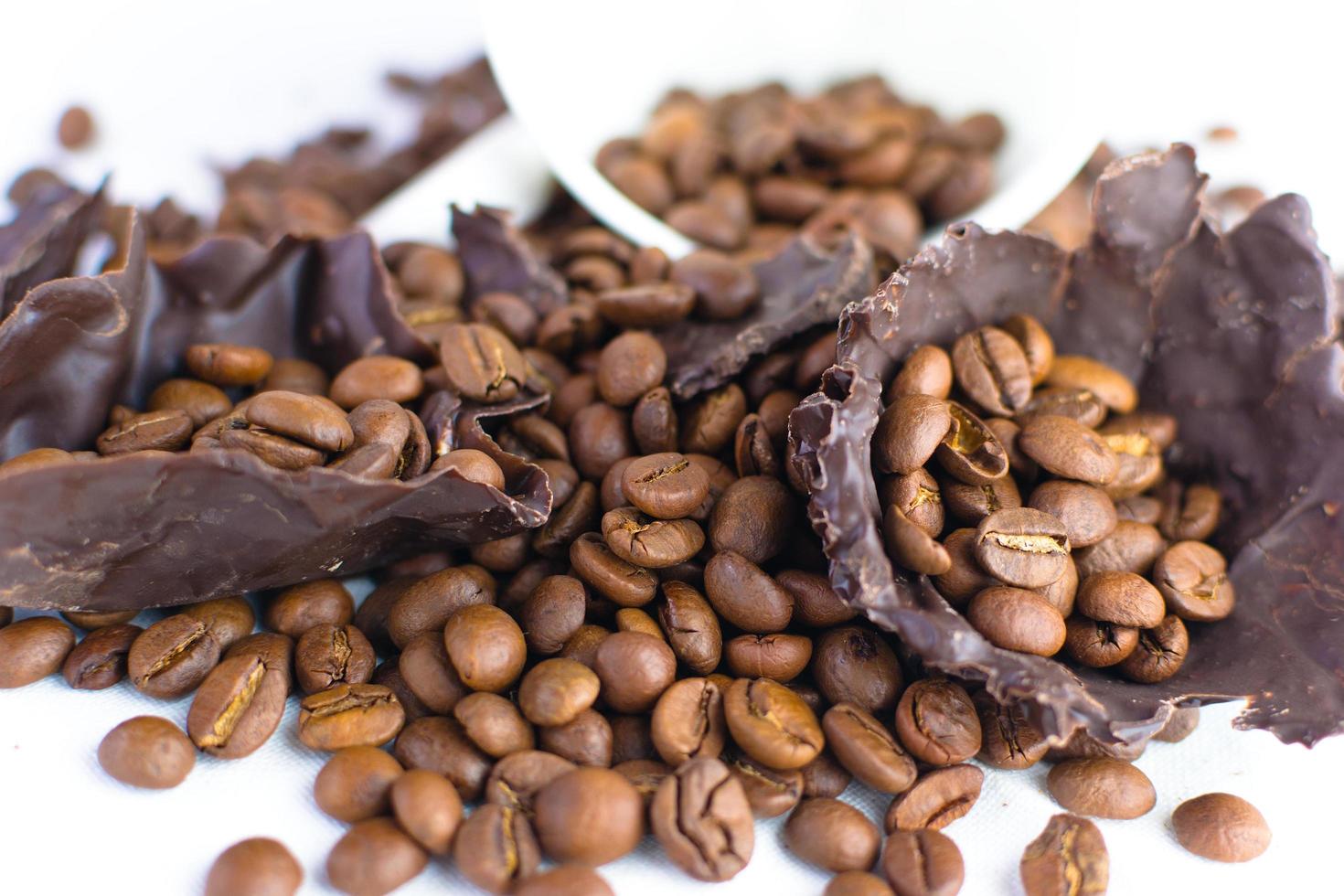 tasse blanche avec des grains de café et des morceaux de chocolat noir sur une nappe blanche photo