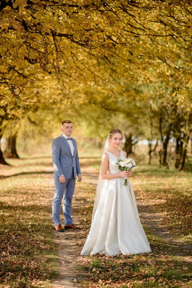 jeune marié et belle mariée dans le parc d'automne. concentrez-vous sur la fille. la jeune fille souffle un bouquet de mariage dans ses mains. photo
