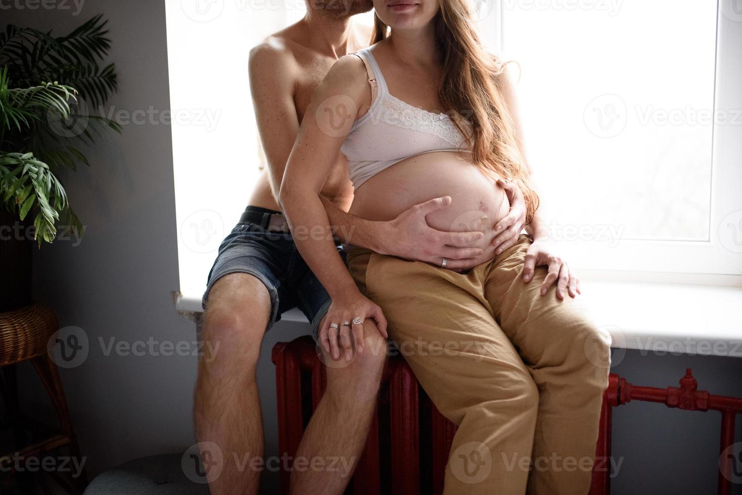 aimer le couple enceinte assis sur le rebord de la fenêtre. auto-isolement d'une maison pendant la quarantaine. photo