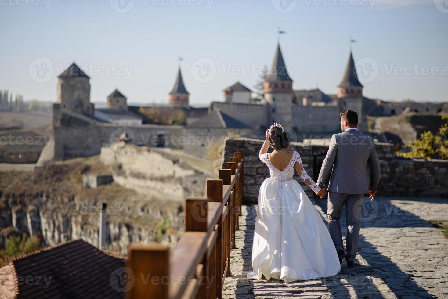 la mariée et le marié se promènent près du vieux château. le couple se tient dos à l'autre. photo