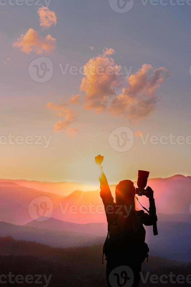 femme voyageuse lève la main pour son succès avec coucher de soleil sur fond naturel de montagnes. photo