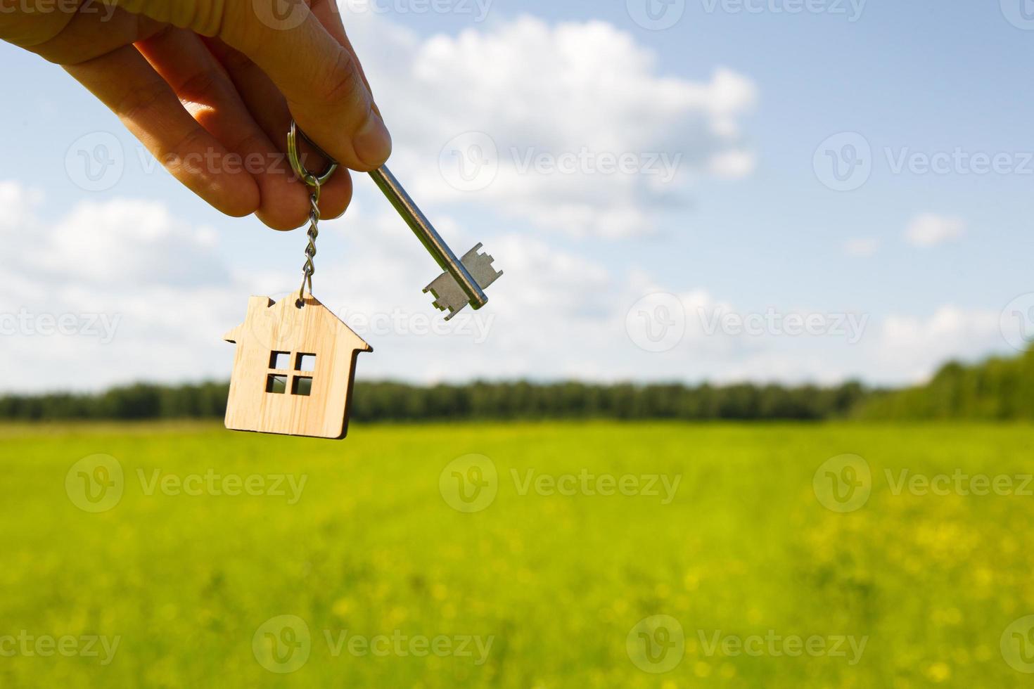 pendentif en bois d'une maison et d'une clé. fond du ciel et du champ. maison de rêve, construction d'un chalet à la campagne, plan et conception, livraison du projet, déménagement dans une nouvelle maison. copie espace photo