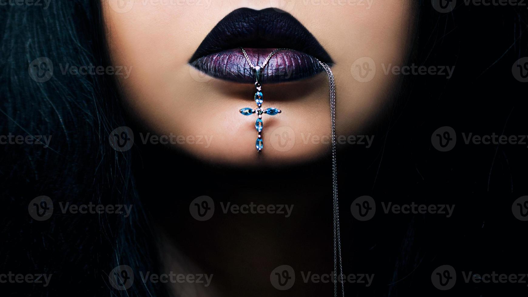 portrait de femme aux cheveux noirs avec des lèvres sombres avec une croix dans la bouche photo