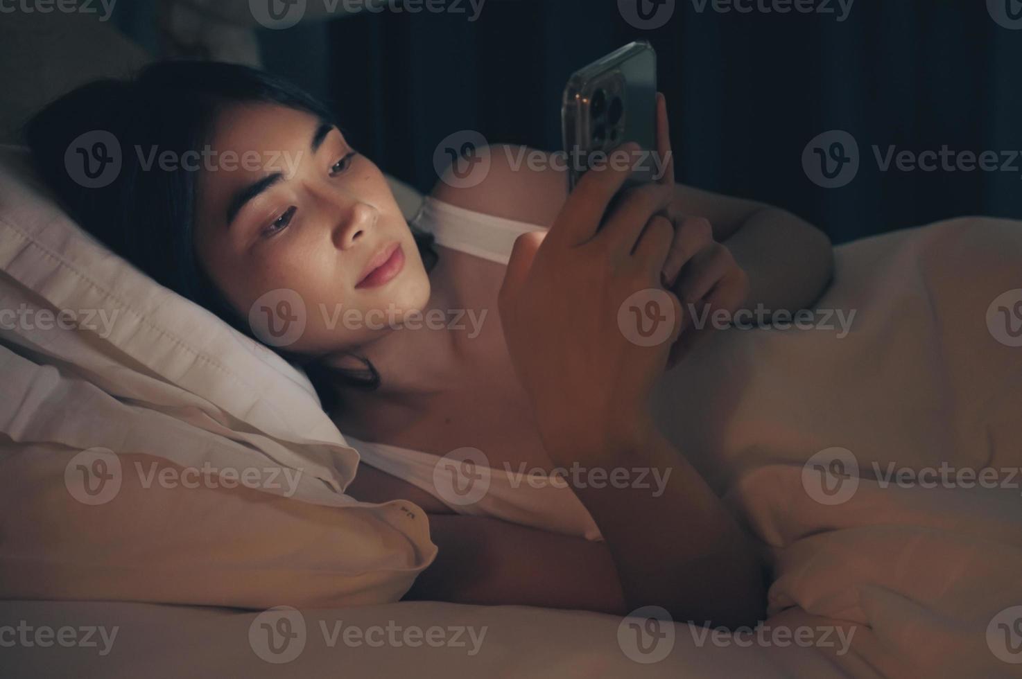 la femme utilise le téléphone sur le lit avant de dormir la nuit. photo