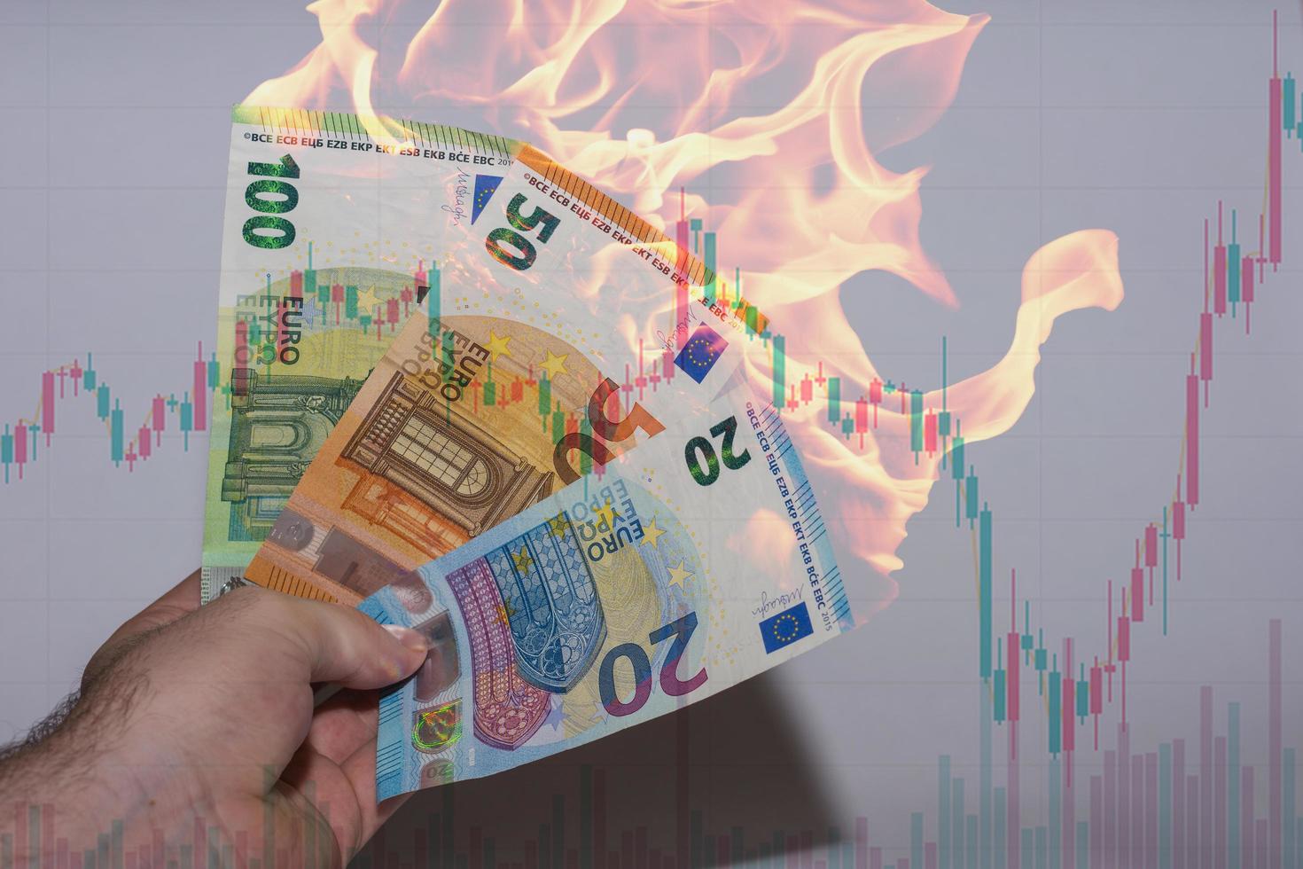 main tenant trois billets de banque en euros brûlants avec un tableau de la finance photo