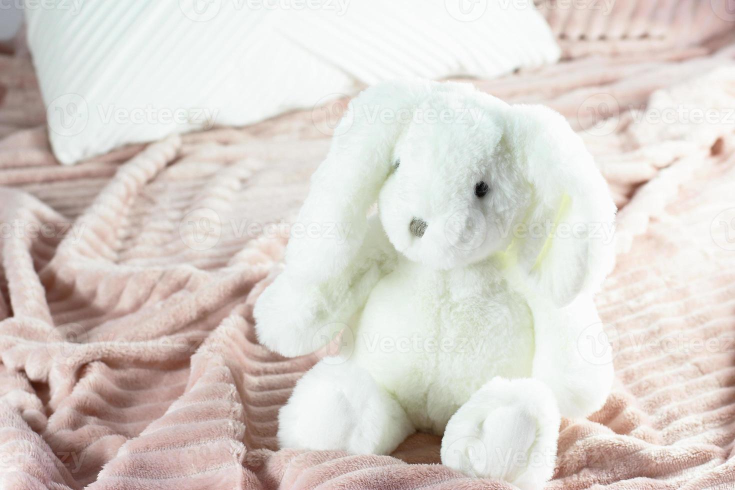 jouet lapin blanc moelleux sur une couverture rose, lapin assis sur le lit photo