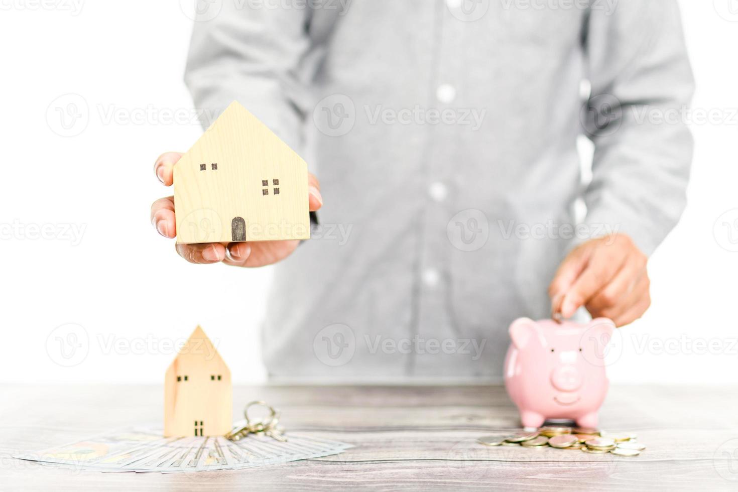 homme d'affaires tenant une maison en bois simulée sur le fond blanc flou dans le bureau avec un espace de copie à gauche. le concept de budget immobilier, pile, argent, pièces de monnaie, dollars. mise au point sélective. photo