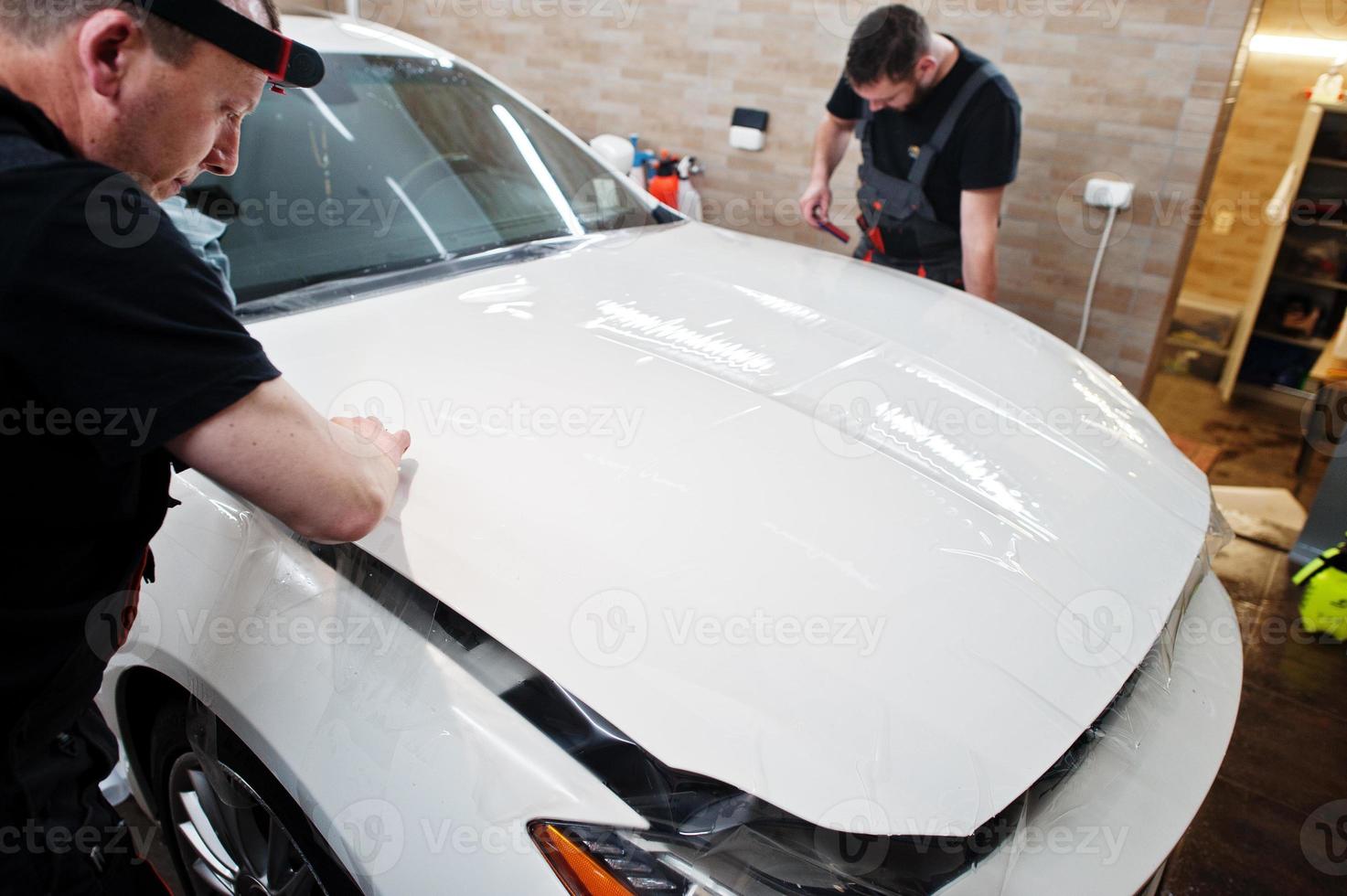 un ouvrier dans un garage de détail a mis une couverture de film anti-gravier en polyuréthane dans une voiture de luxe blanche. photo