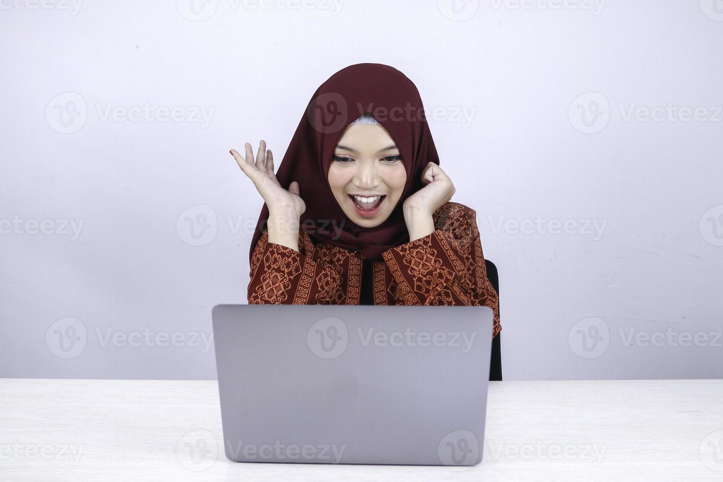 la jeune femme islamique asiatique portant le foulard est choquée et excitée par ce qu'elle voit sur l'ordinateur portable sur la table. photo