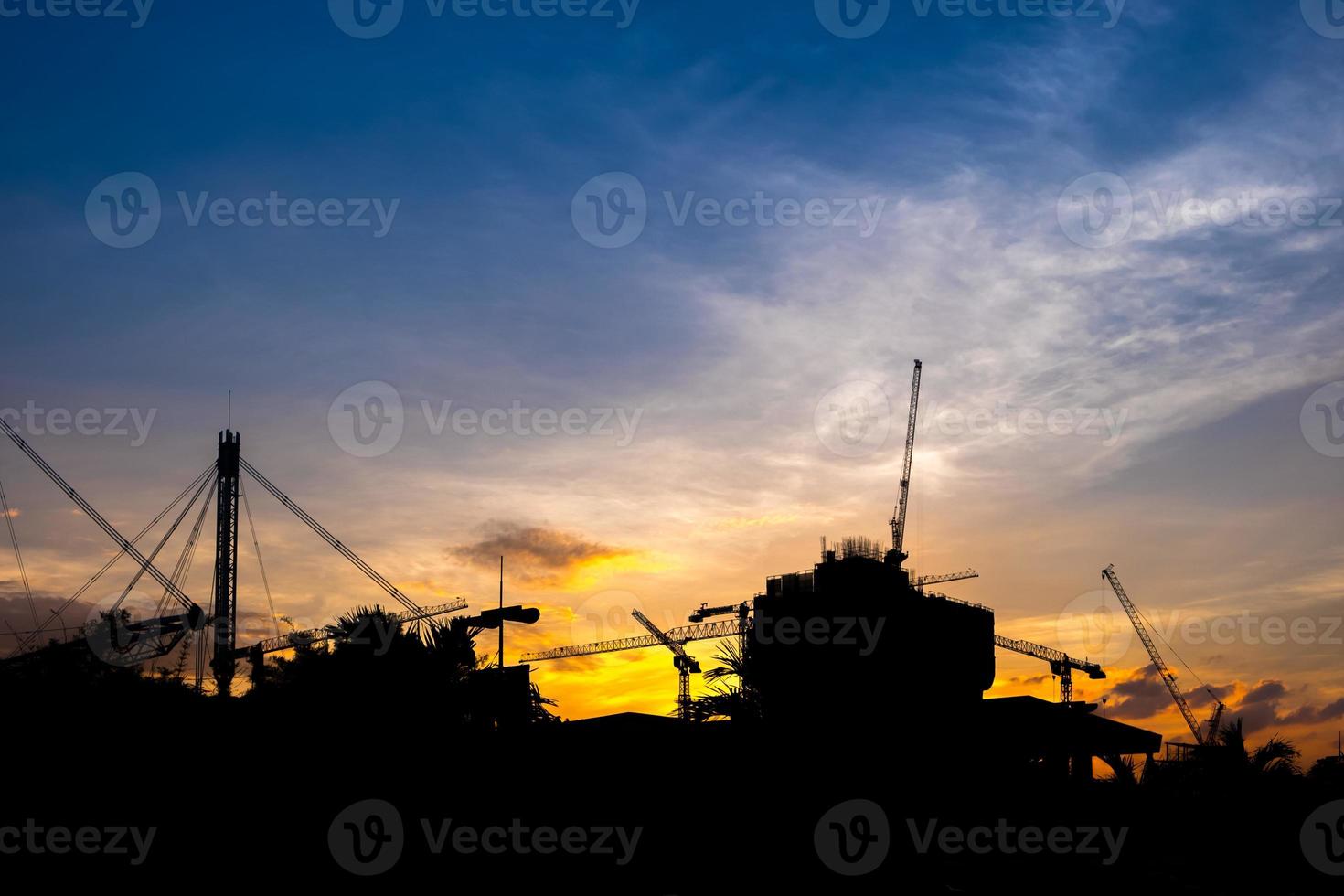 grues de construction industrielle et silhouettes de bâtiments au coucher du soleil photo
