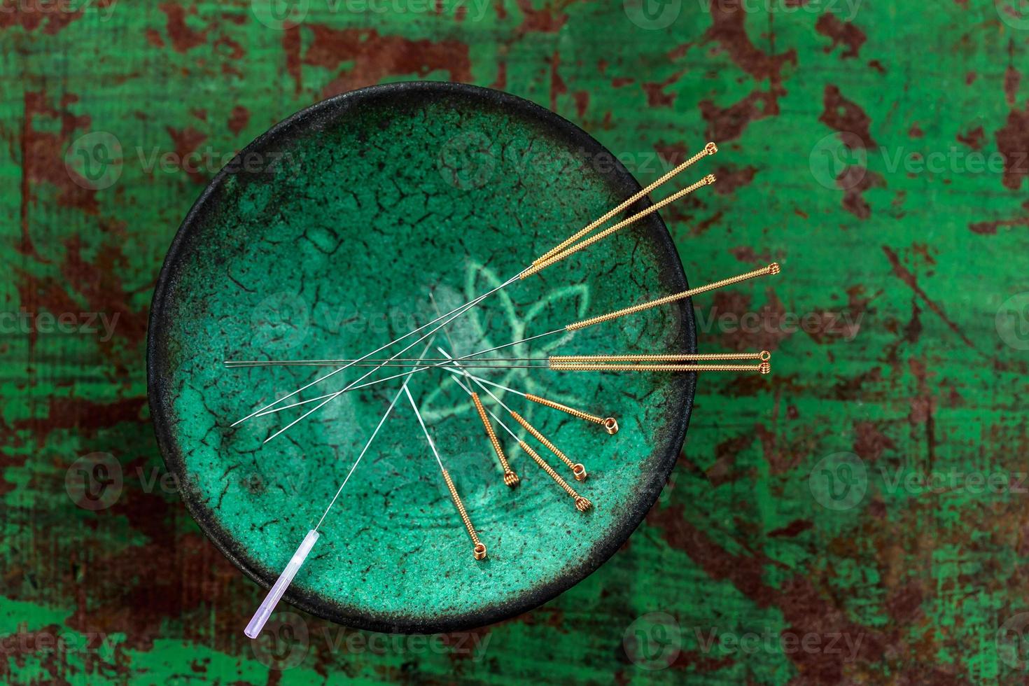 bol asiatique en céramique verte avec des aiguilles pour l'acupuncture sur un vieux fond de bois de peinture verte photo