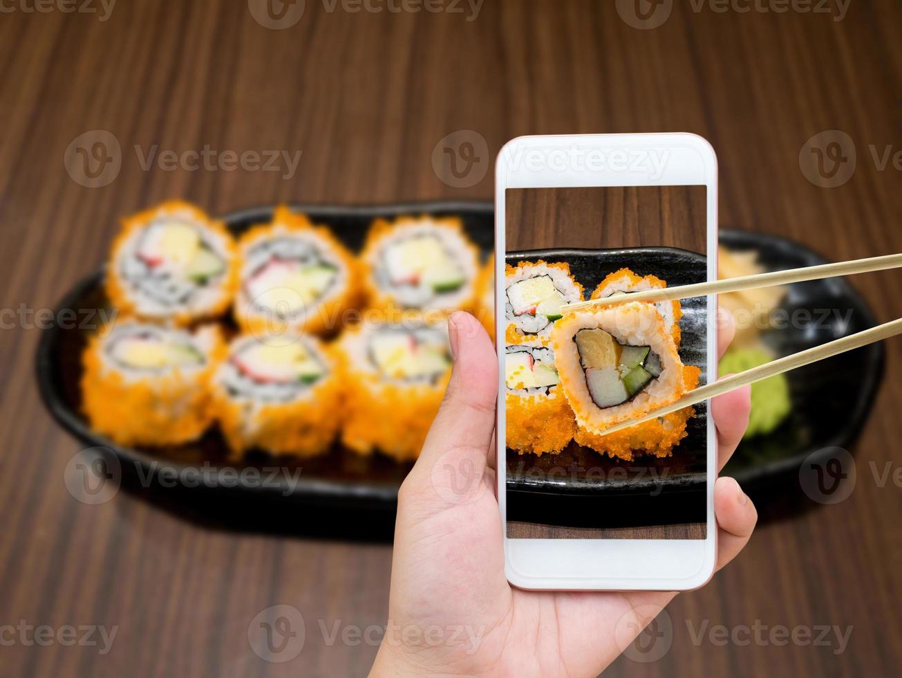 main féminine prenant une photo de maki sushi avec un téléphone portable