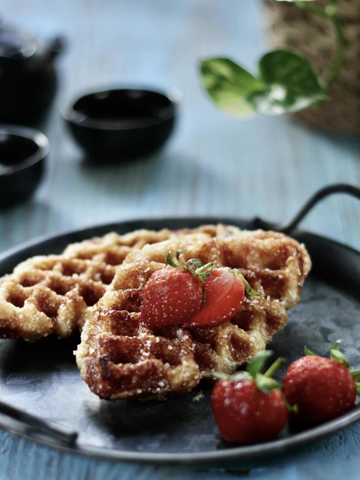 vue en grand angle de croffle, plats modernes à emporter ou à livrer, servis avec des fraises sur l'assiette vintage et la table bleue. photo