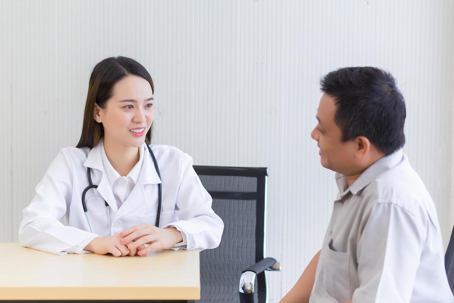 jeune femme médecin professionnelle asiatique sourire de bonne humeur suggère des solutions de santé aux patients masculins âgés dans la salle d'examen de l'hôpital. photo