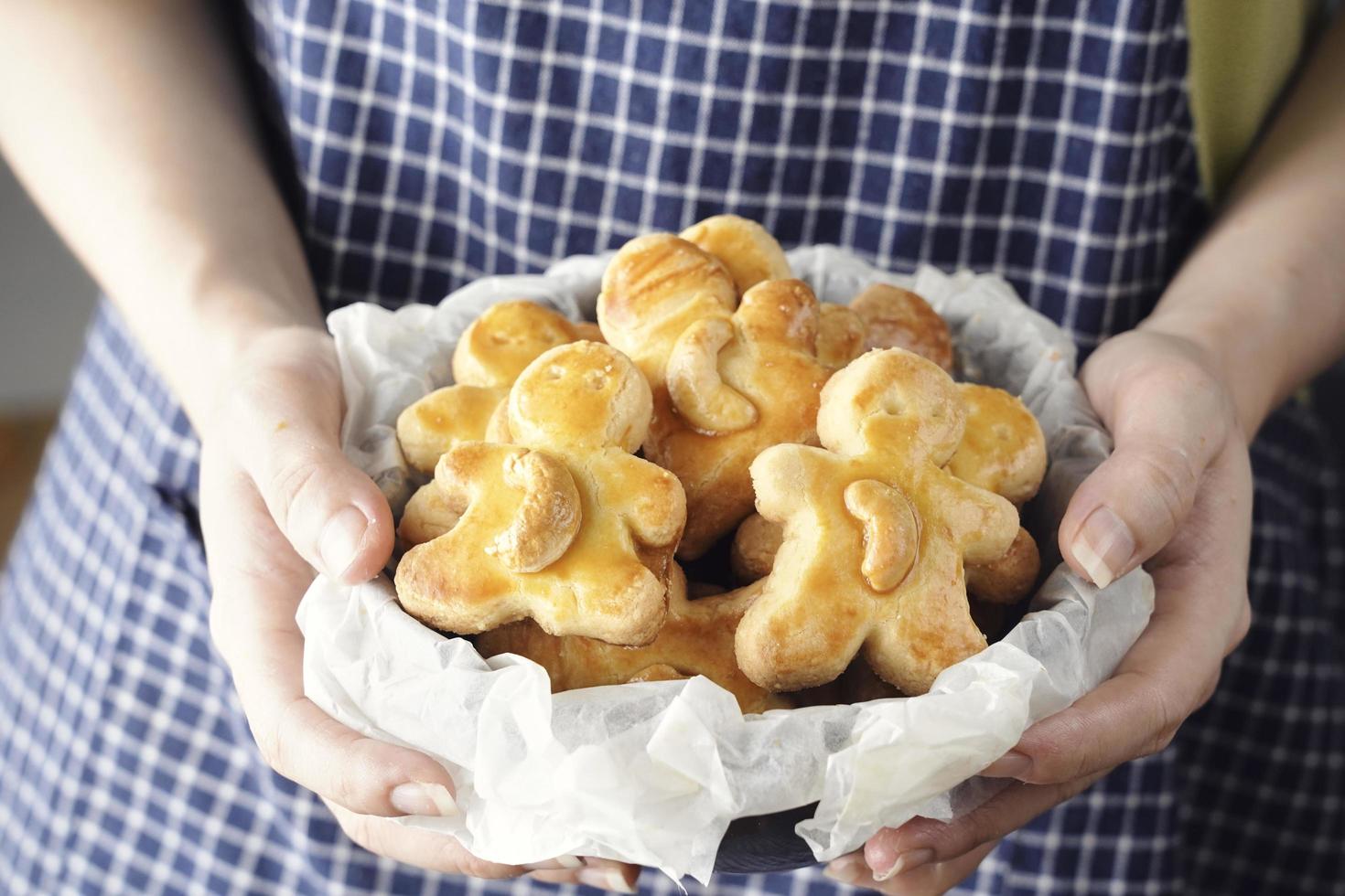 mains de femme tenant des biscuits de noël faits maison, des biscuits aux noix de cajou fraîchement cuits en forme de poupée sur un tableau blanc photo