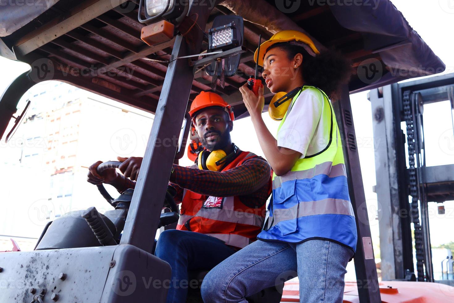 les travailleurs industriels portent un gilet de sécurité et un casque conduisant un chariot élévateur dans l'industrie de l'usine, deux ingénieurs afro-américains, homme et femme, travaillent ensemble dans un parc à conteneurs de fret logistique. photo