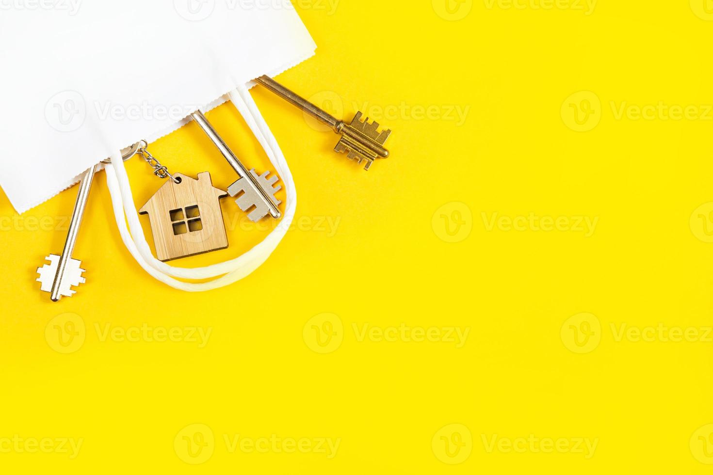 porte-clés en forme de maison en bois avec clé sur fond jaune dans un emballage cadeau en papier blanc. hypothèque, location et achat immobilier, offre avantageuse pour la construction. copie espace photo