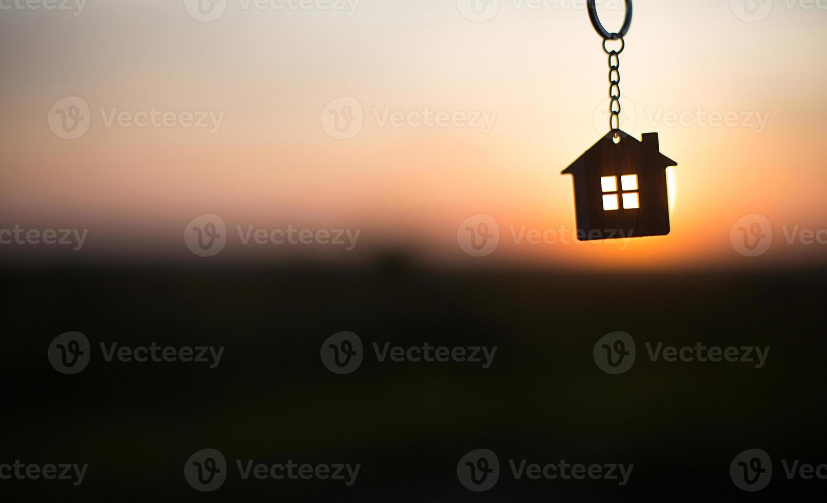silhouette d'une figure de maison avec une clé, un stylo avec un porte-clés sur fond de coucher de soleil. ils rêvent d'une maison, de construire, d'emménager dans une nouvelle maison, d'hypothèques, de louer et d'acheter un bien immobilier photo