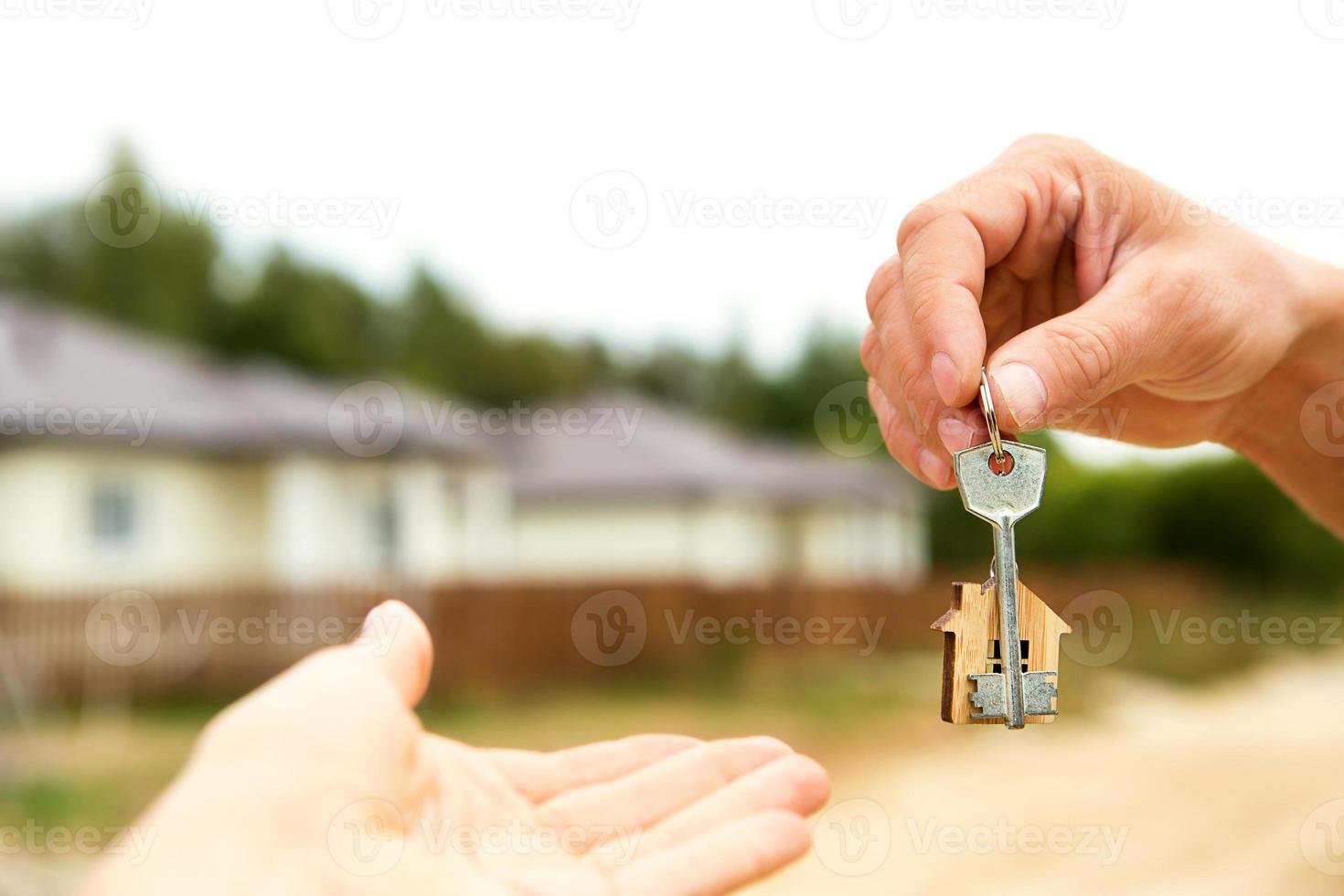 main avec une clé et un porte-clés en bois. fond de clôture et de chalet. construction, projet, emménagement dans une nouvelle maison, hypothèque, location et achat immobilier. pour ouvrir la porte. copie espace photo