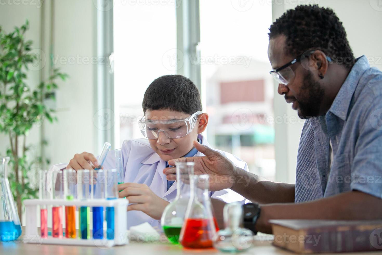 petit garçon mélange des produits chimiques dans des béchers. un enseignant enthousiaste explique la chimie aux enfants, un étudiant en chimie montre une nouvelle expérience au cours de sciences de l'enseignant photo