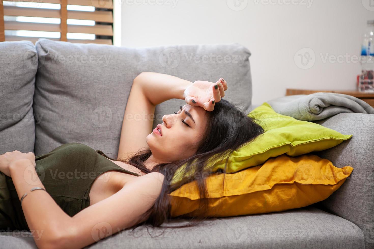 triste jeune femme déprimée à la maison assise sur un canapé. fille frustrée et malheureuse avec de terribles migraines ou maux de tête. photo