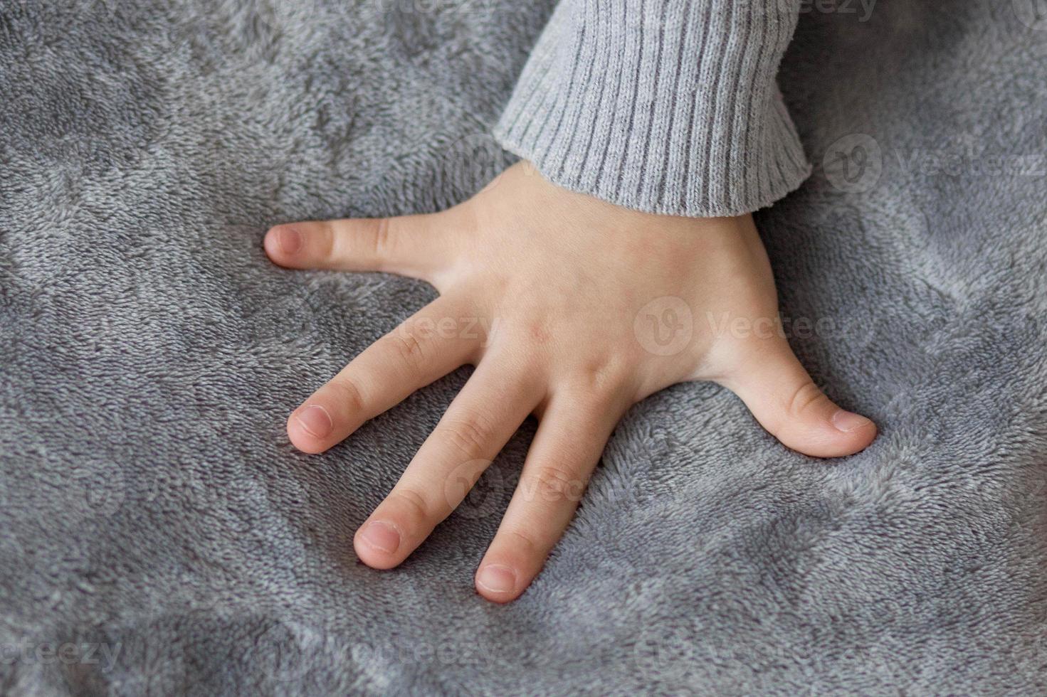 main d'enfant sur fond gris. la main d'une fille avec les doigts tendus sur un tissu en peluche gris photo