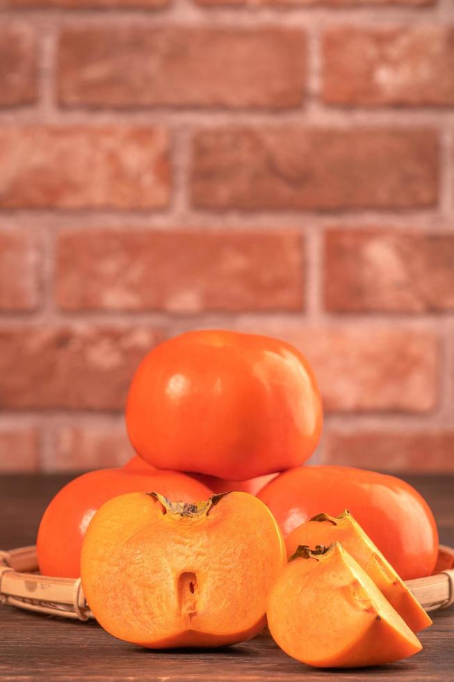 Kaki de kaki doux frais et tranché sur une table en bois sombre avec fond de mur de briques rouges, concept de design de fruits du nouvel an lunaire chinois, gros plan. photo