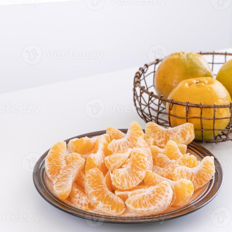 belles mandarines pelées dans une assiette et un panier en métal isolés sur une table blanche et propre dans un îlot de cuisine contemporain moderne, gros plan. photo