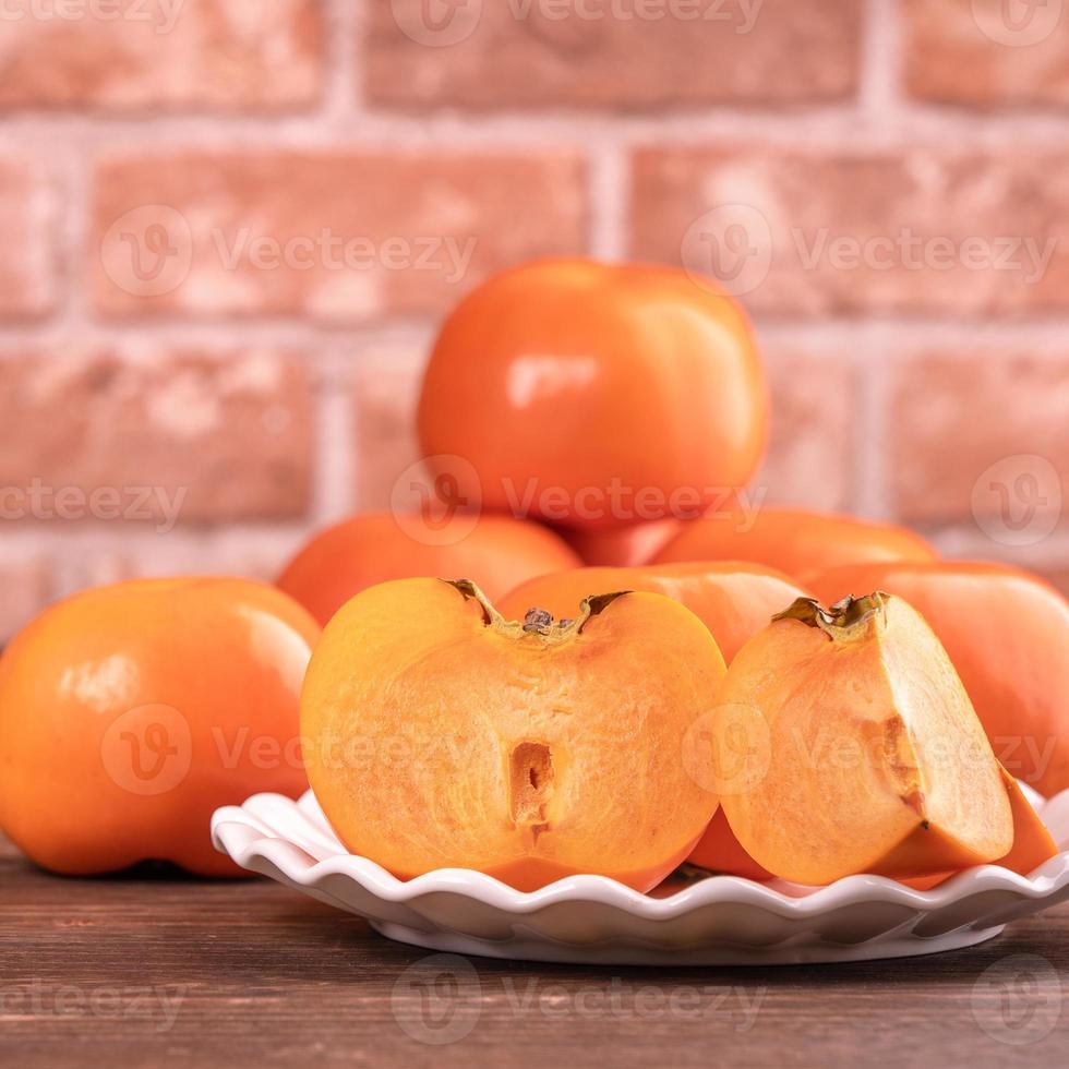 Kaki de kaki doux frais et tranché sur une table en bois sombre avec fond de mur de briques rouges, concept de design de fruits du nouvel an lunaire chinois, gros plan. photo