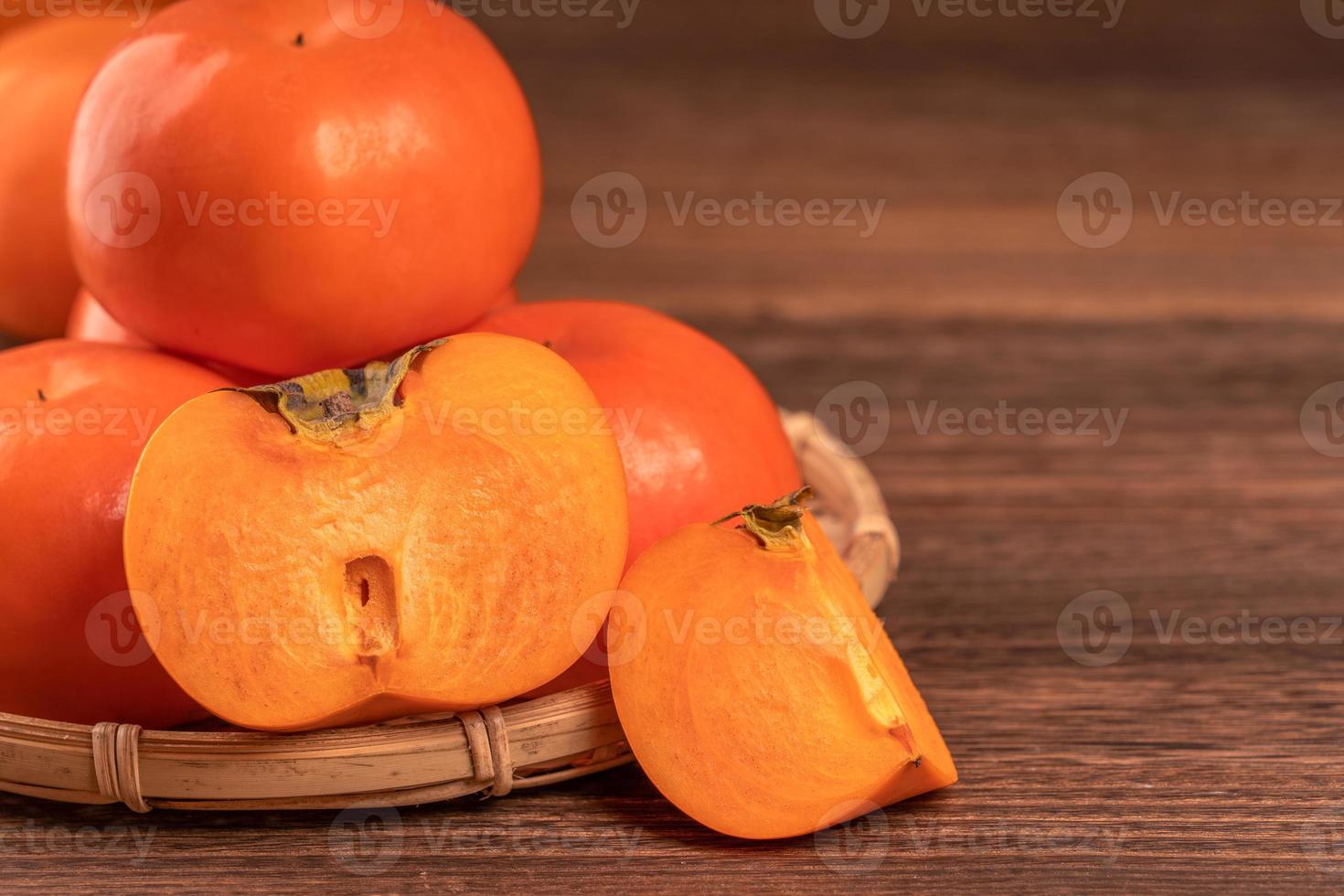 kaki de kaki sucré tranché dans un panier de tamis en bambou sur une table en bois sombre avec fond de mur de briques rouges, concept de conception de fruits du nouvel an lunaire chinois, gros plan. photo