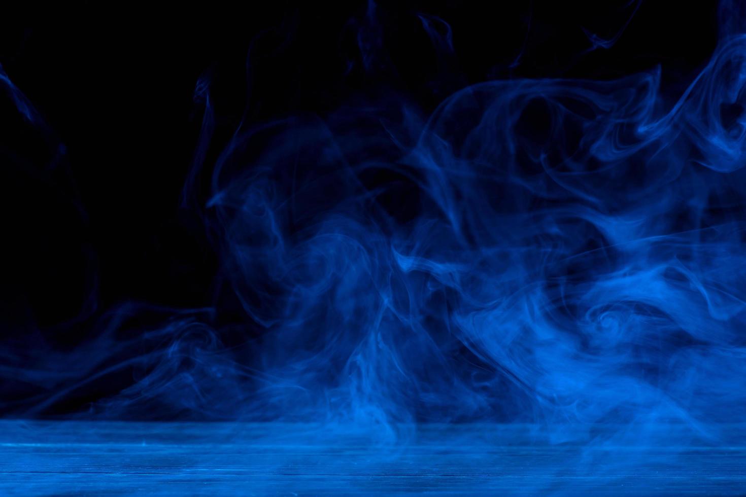 image conceptuelle de fumée bleue isolée sur fond noir foncé et table en bois. photo