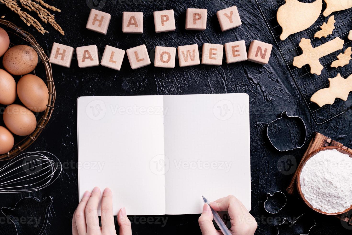 la jeune femme lit et écrit la recette de la fabrication de biscuits d'halloween, le concept de conception de la préparation de la fête d'halloween, la vue de dessus, la pose à plat, les frais généraux. photo