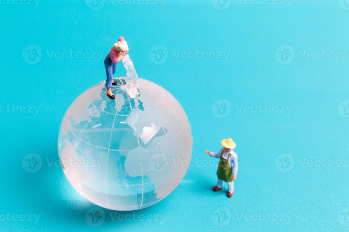 personnes miniatures nettoyant un globe de cristal sur fond bleu photo