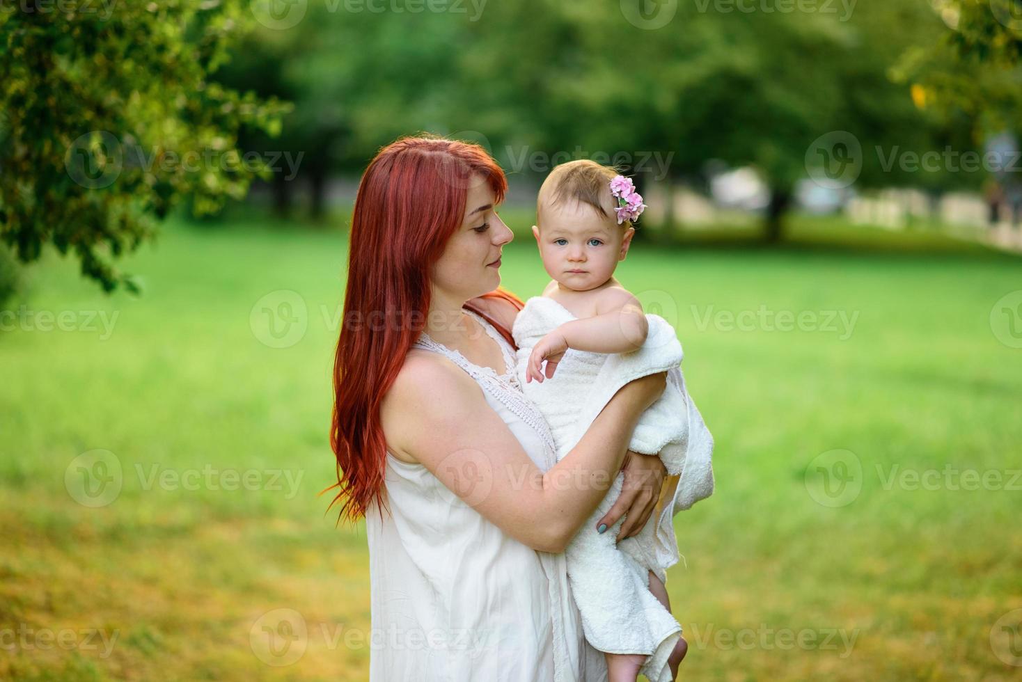 maman embrasse et joue avec sa fille d'un an enveloppée dans une serviette après le bain. photo