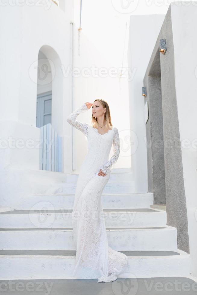 la belle jeune femme aux cheveux blonds mariée bleue dans une longue robe sexy blanche de mariage à santorin en grèce photo