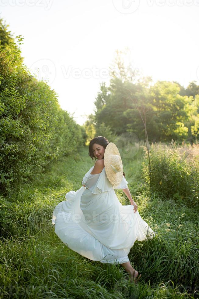 femme enceinte au chapeau posant dans une robe sur fond d'arbres verts. photo