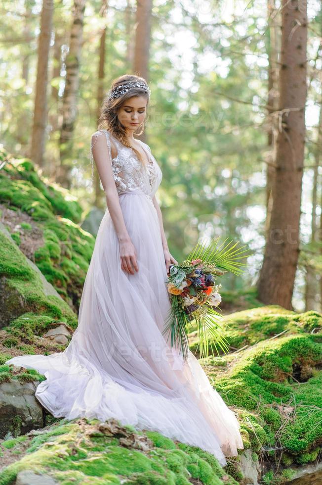 mariée heureuse dans une robe de mariée rose. la jeune fille tient un bouquet de mariage dans ses mains. cérémonie de mariage de style bohème dans la forêt. photo