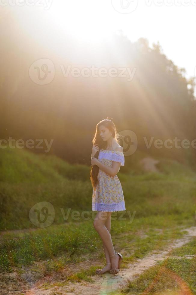 portrait d'une belle jeune fille en robe d'été. séance photo d'été dans le parc au coucher du soleil. une fille est assise sous un arbre à l'ombre.