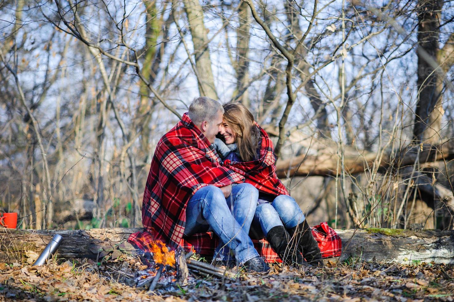 jeune couple aimant vêtu d'un pull bleu assis avec des tasses à café rouges sur le bois de chauffage dans la forêt d'hiver photo