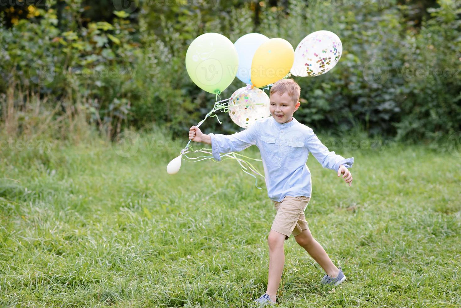 un garçon d'âge scolaire court avec des ballons. le garçon fête son anniversaire dans le parc. photo