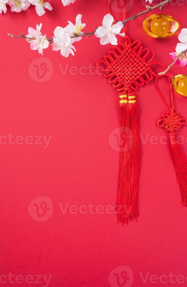 concept de design du nouvel an lunaire chinois - beau noeud chinois avec fleur de prunier isolé sur fond rouge, mise à plat, vue de dessus, mise en page aérienne. photo