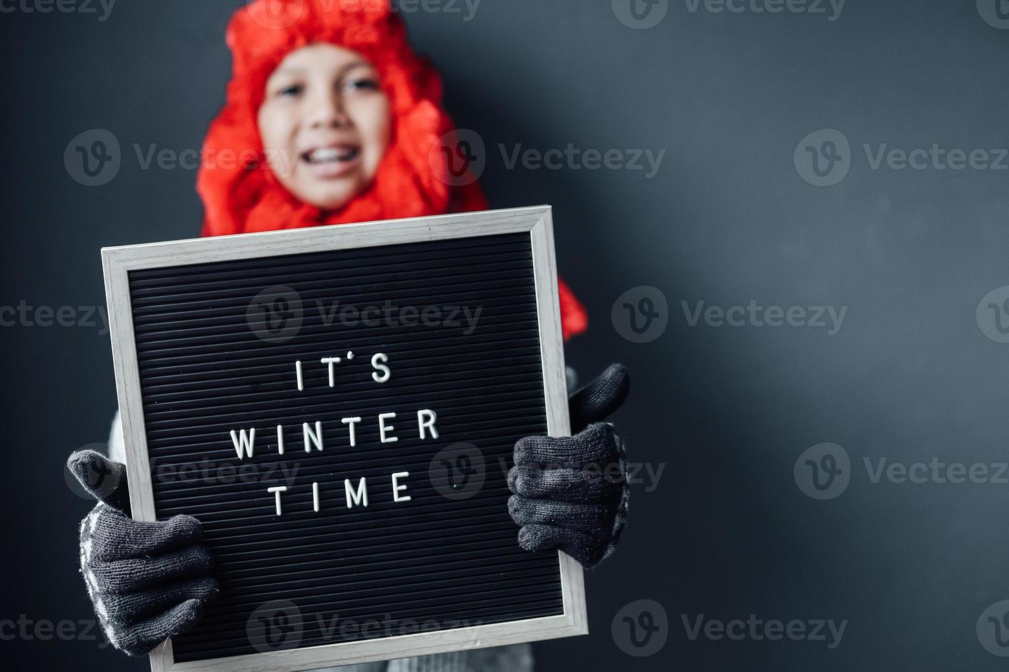 mignon garçon avec une expression heureuse portant des vêtements d'hiver se félicite de la saison d'hiver photo