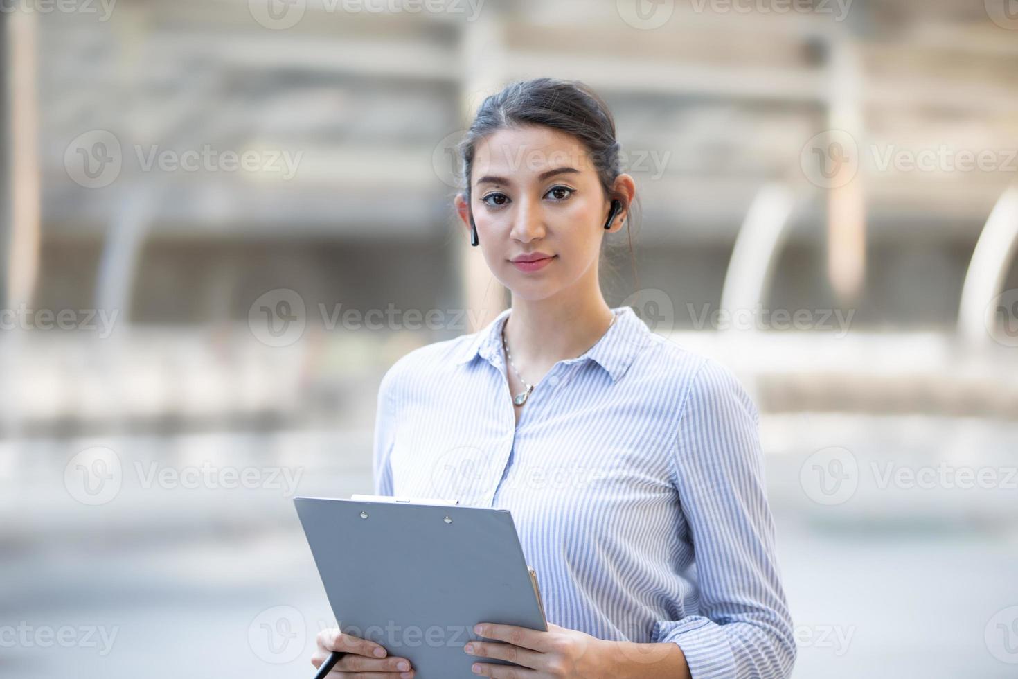 jeune femme d'affaires avec écouteur tenant le presse-papiers debout à l'extérieur. photo