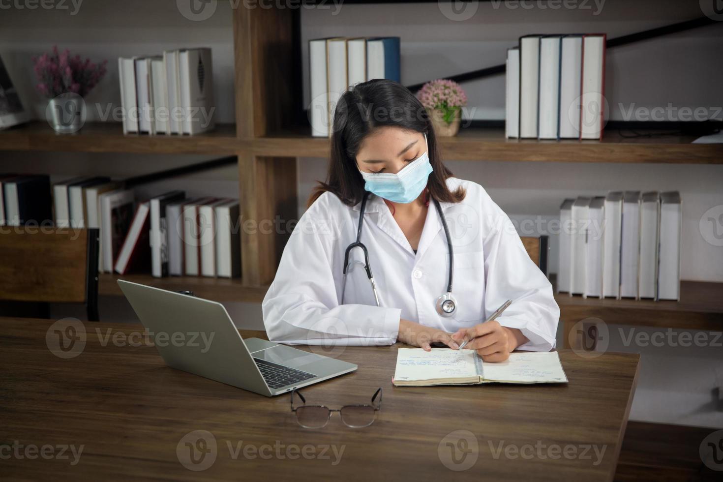 femme médecin asiatique utilisant un ordinateur portable par fenêtre dans son bureau. photo