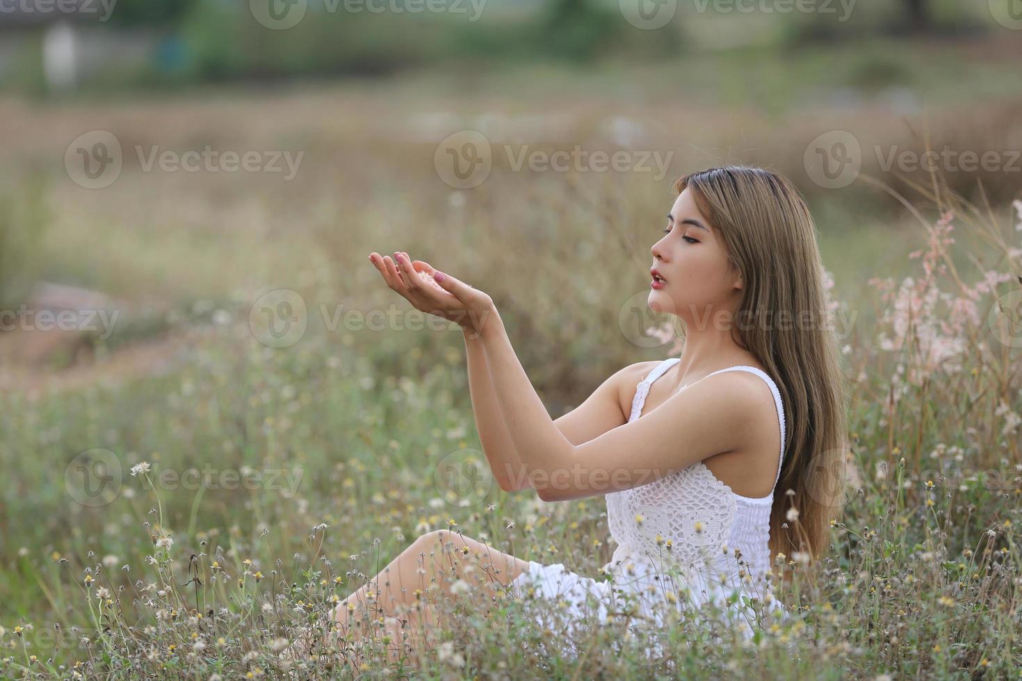 belle jeune femme assise sur le terrain dans l'herbe verte et pissenlit soufflant. en plein air. profiter de la nature. fille souriante en bonne santé sur la pelouse de printemps. concept sans allergie. liberté photo